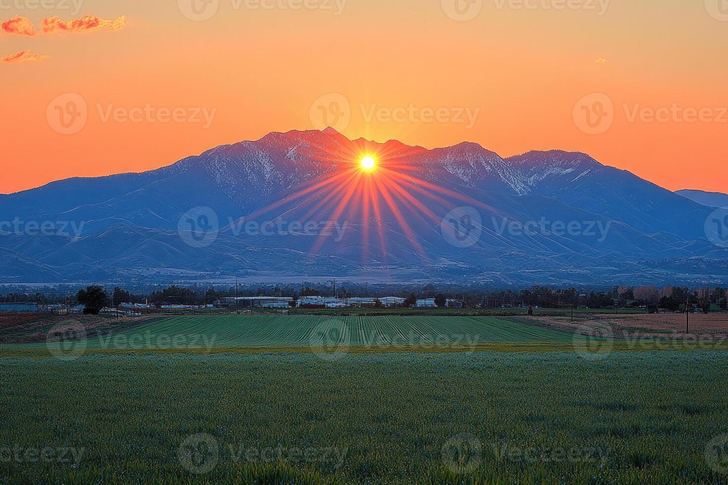 Sun Setting Behind A Mountain Range With Sunbeams Over Field photo
