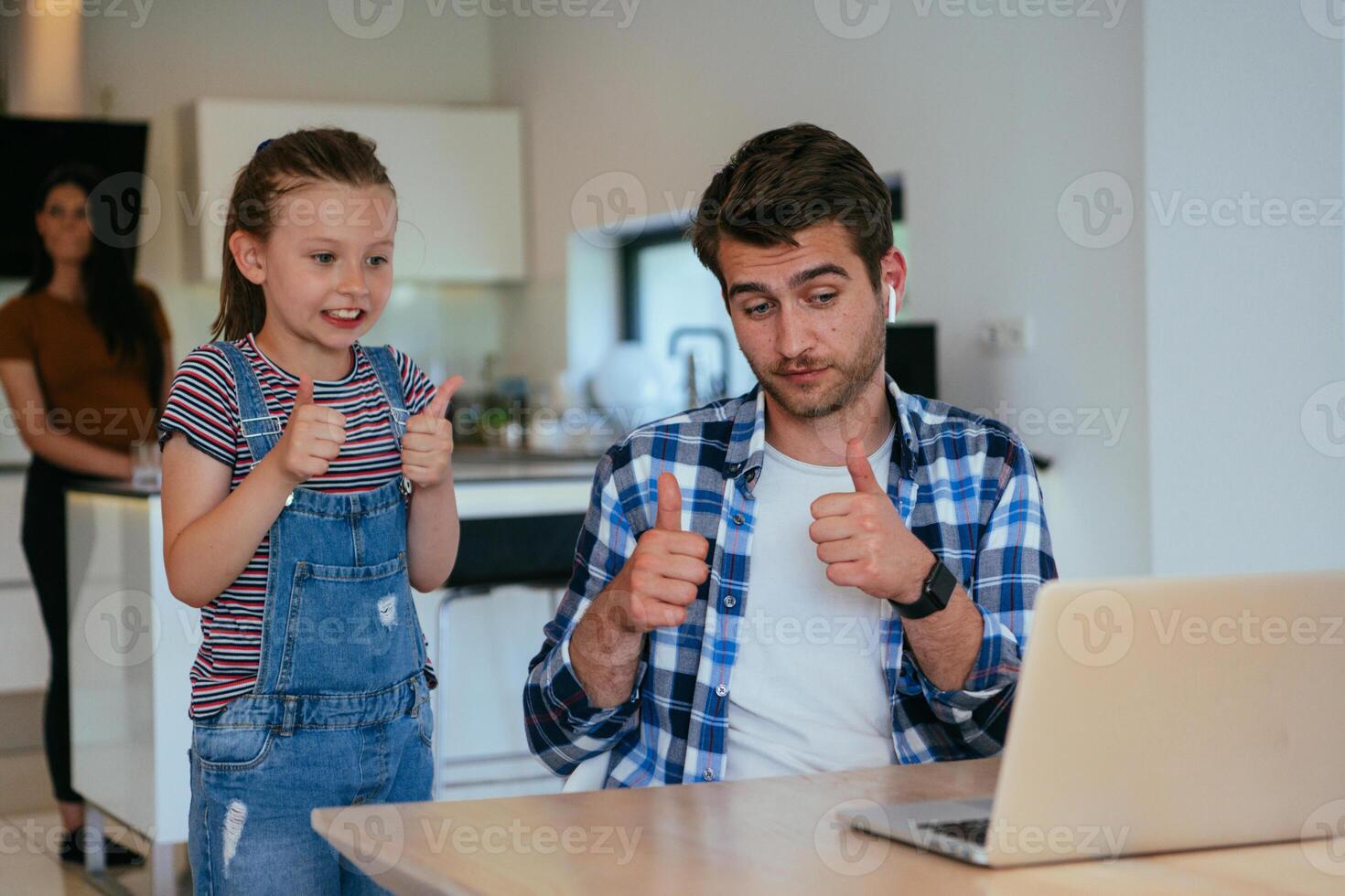 Work from home. Daughter interrupting her father while he is having a business online conversation on his laptop while sitting in the modern living room. photo
