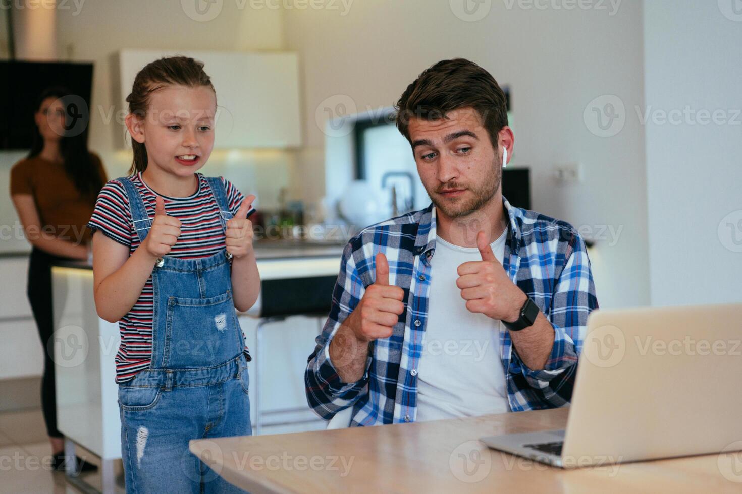 Work from home. Daughter interrupting her father while he is having a business online conversation on his laptop while sitting in the modern living room. photo