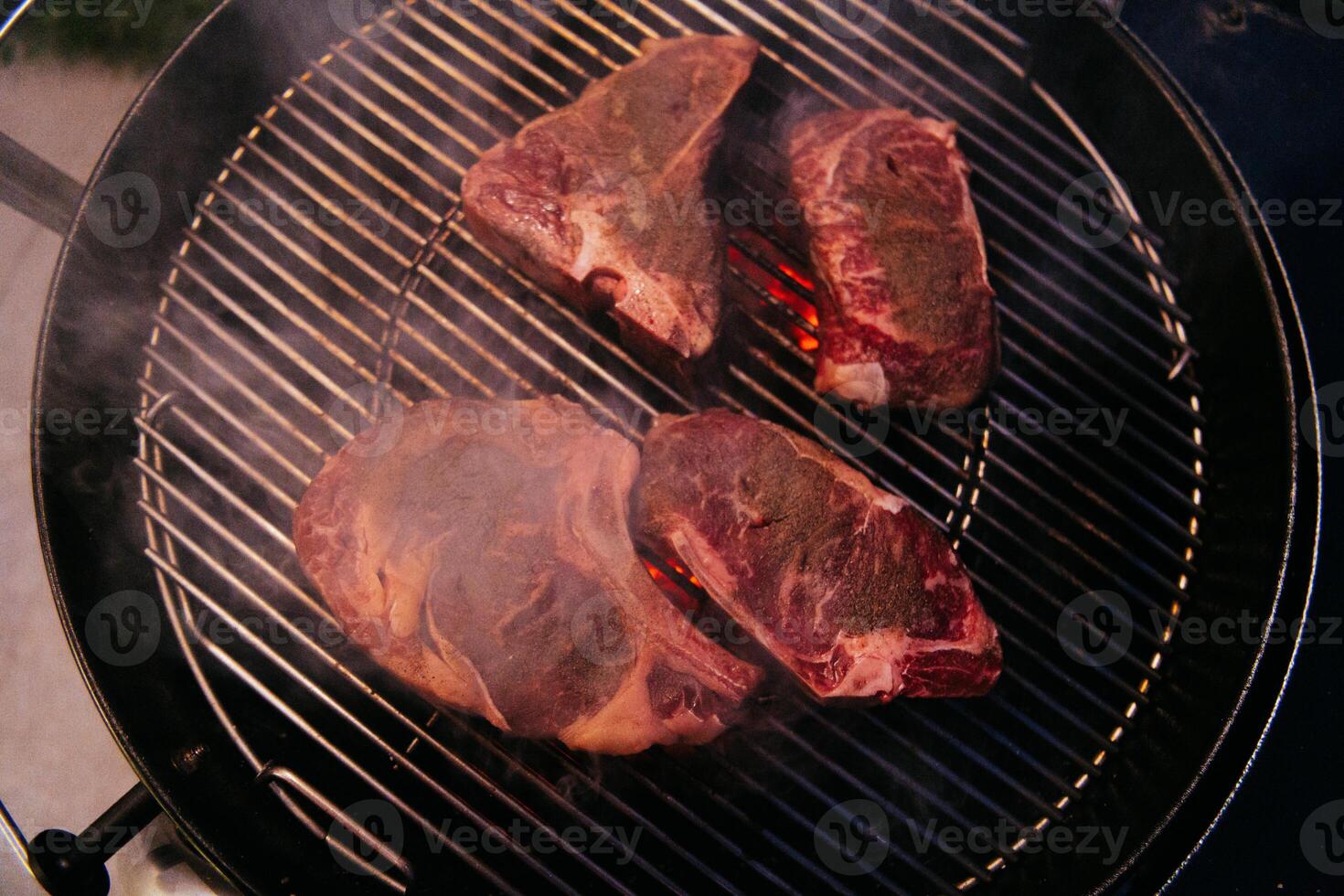 Close-up photo of delicious meat being grilled. In the background, friends and family are sitting and waiting for a meal.