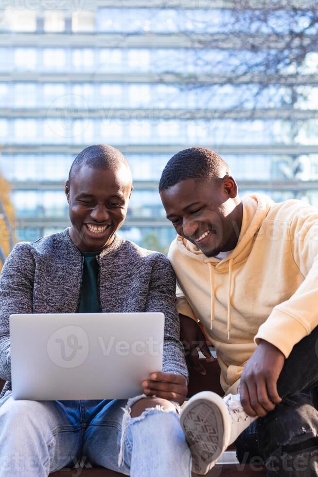 Smiling black men using laptop while sitting on bench. photo