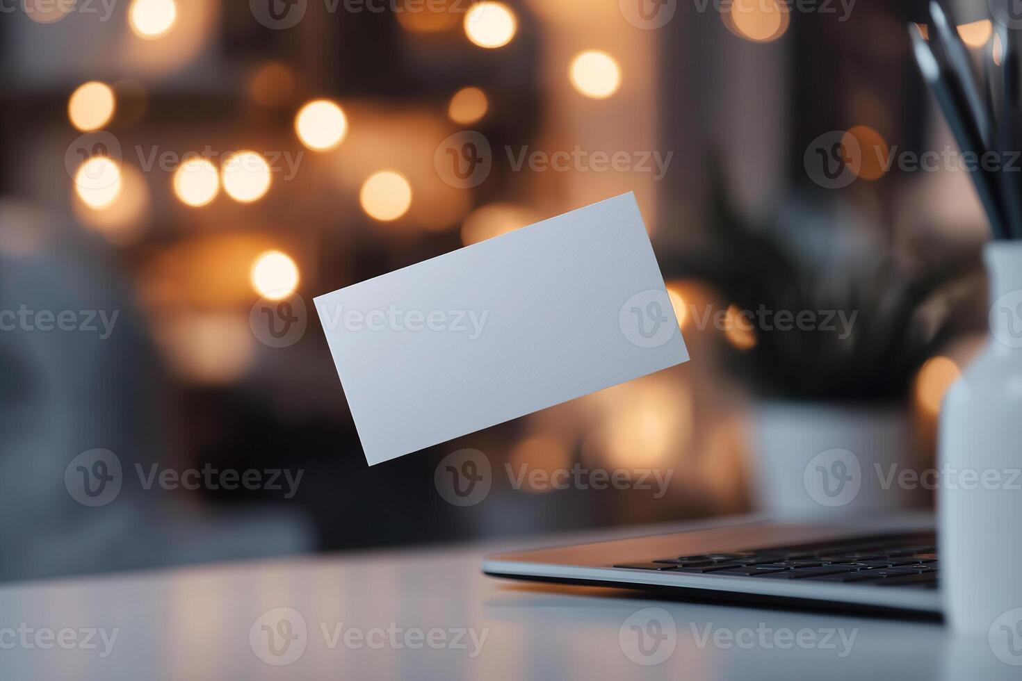 A blank business card hovers above a laptop keyboard in a sleek workspace. Soft lighting enhances the high-tech atmosphere, ideal for startups and digital branding photo