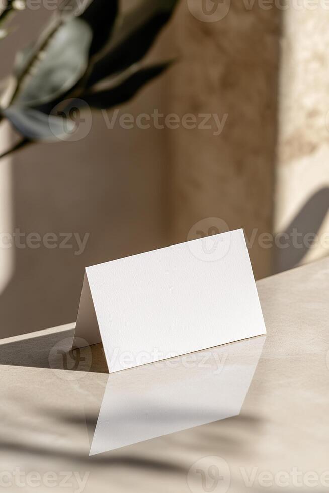 A blank business card stands upright against a neutral-toned wall, slightly leaning. The soft reflections and blurred background create an aesthetic, upscale ambiance ideal for luxury branding photo