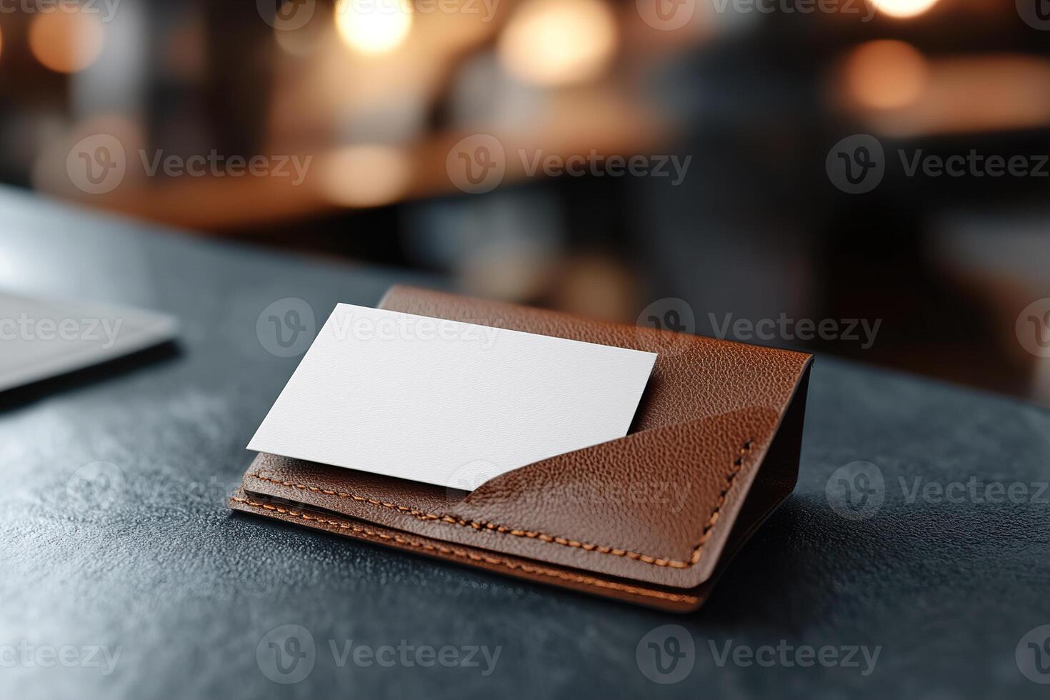 A blank business card is partially tucked into a fine-grain leather cardholder, reflecting soft lighting. The blurred backdrop suggests a sophisticated executive workspace, perfect for branding photo