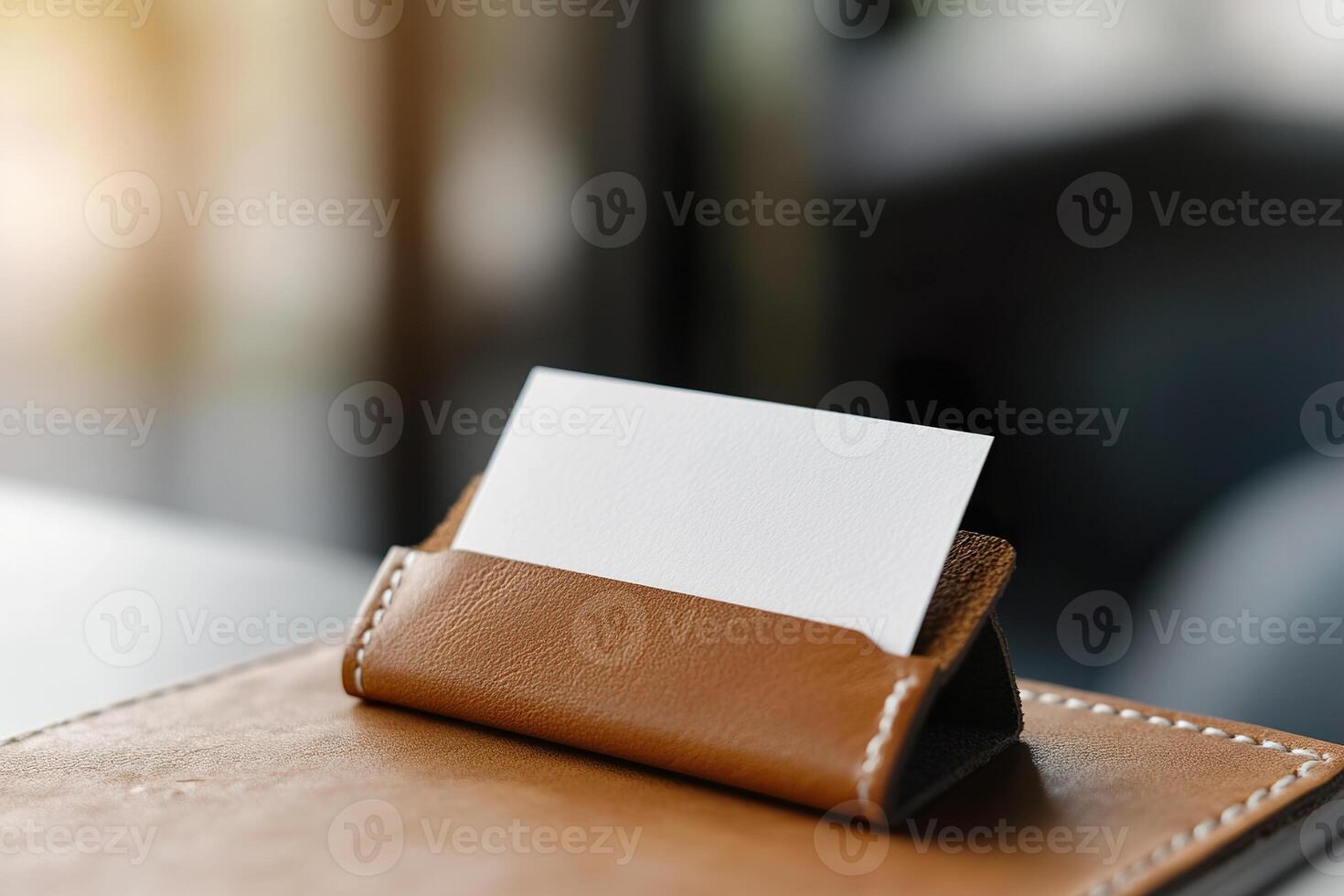 A blank business card is partially visible in a high-quality leather cardholder, resting on a desk with soft lighting creating an elegant atmosphere suitable for corporate branding photo