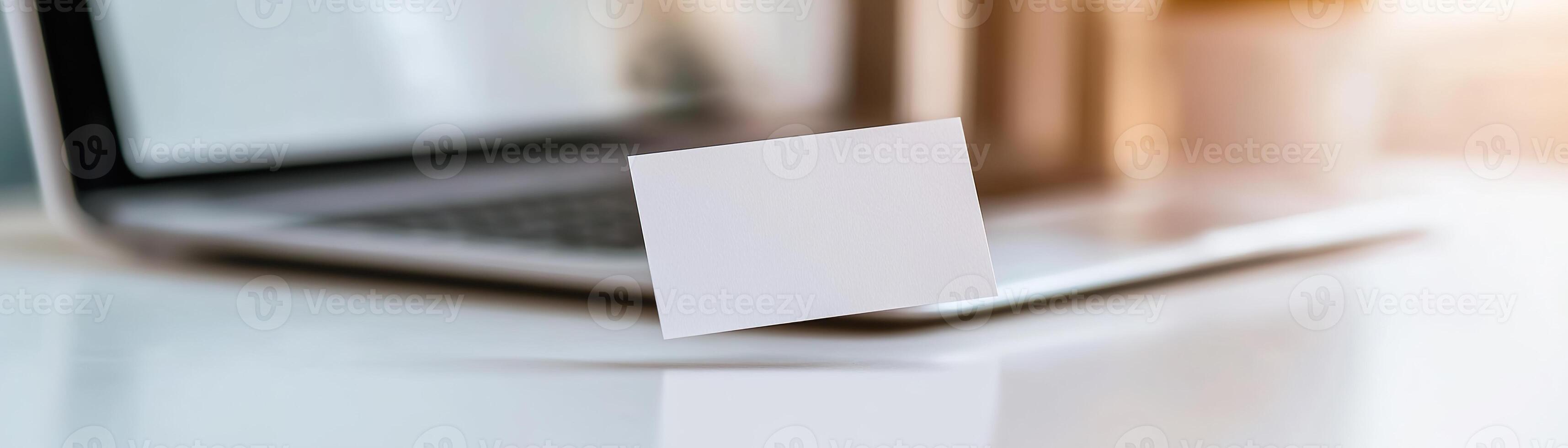 A blank business card hovers just above a sleek laptop keyboard, illuminated by soft lighting, in a high-tech workspace photo