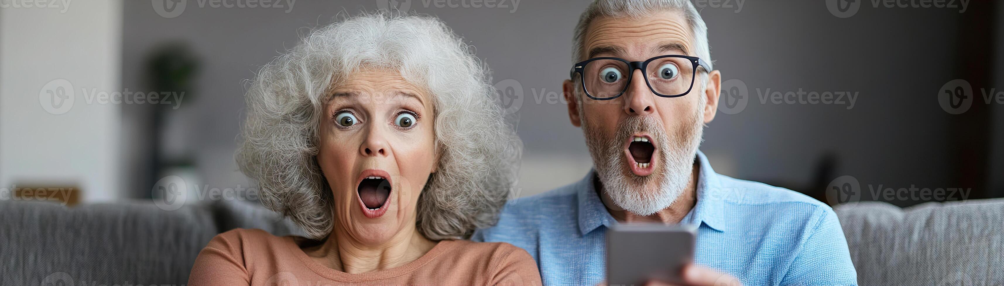 A joyful senior couple sits closely together, their expressions filled with surprise as they look at a smartphone photo
