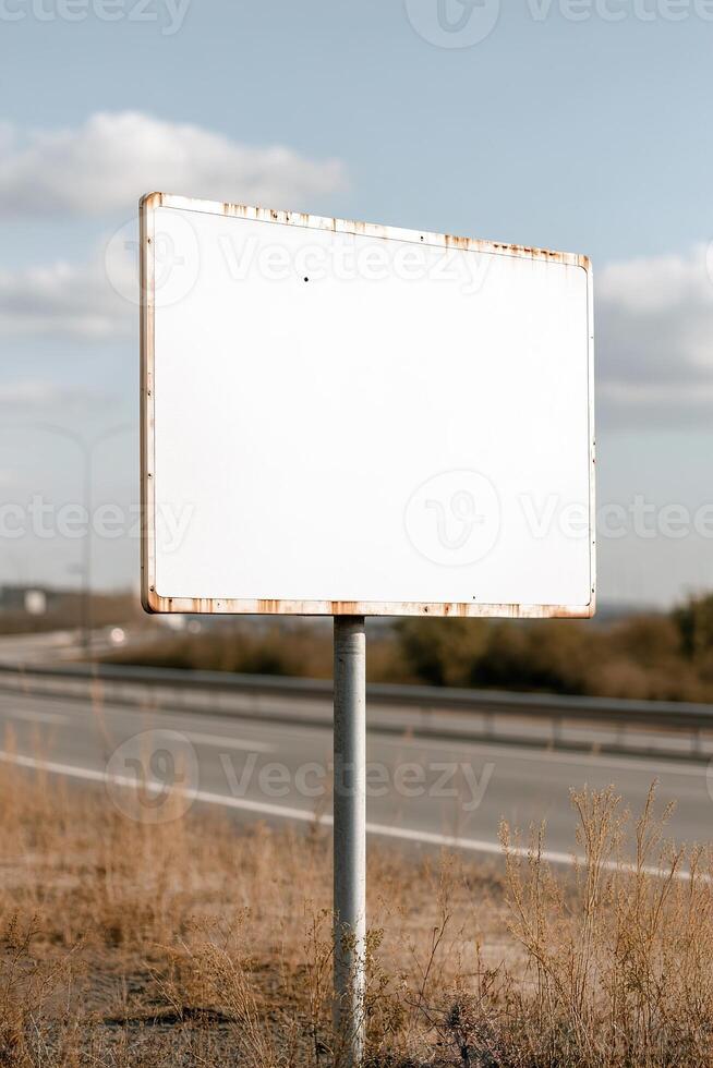 A large blank signboard is mounted on a sturdy metal pole beside a wide highway photo