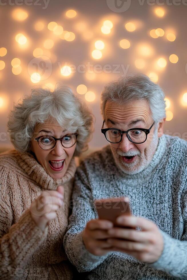 Senior couple expresses delight while looking at a smartphone together in a warm, inviting home. The cozy atmosphere enhances their joyful interaction as they explore new tech photo