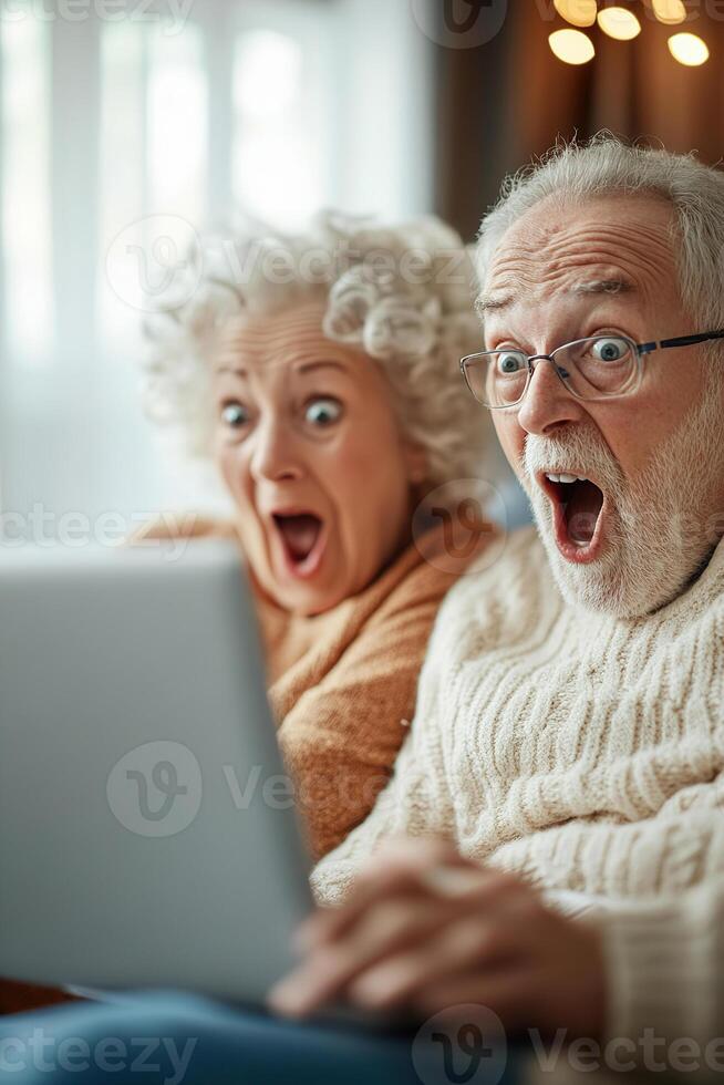 A senior couple shares a moment of surprise and delight as they explore a laptop together on their couch in a bright living room. Their expressions reflect joy and curiosity in this inviting setting photo