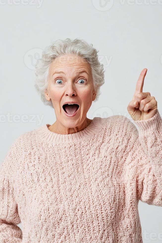 A lively senior woman in a casual sweater expresses surprise and excitement while pointing to the right. Her enthusiasm shines through, making it perfect for engaging promotional content photo