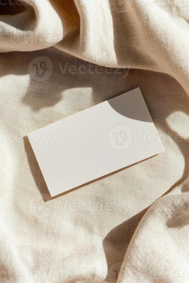 A blank business card lies on wrinkled linen fabric, showcasing natural textures and shadows. The warm earthy background enhances its elegant and refined appeal for various brands photo