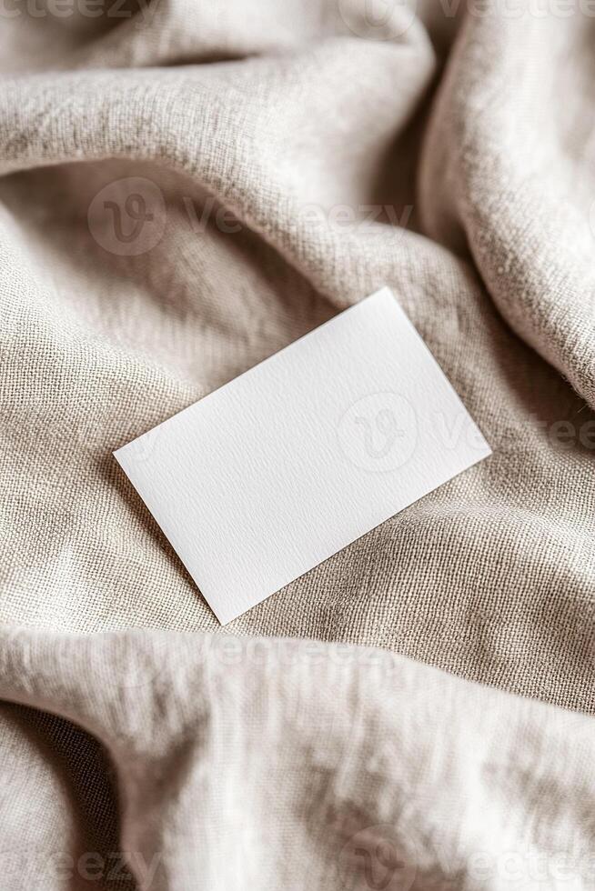 A blank business card rests on soft, textured linen, highlighting gentle folds and shadows. The warm background offers an earthy tone, ideal for eco-friendly branding and boutique aesthetics photo