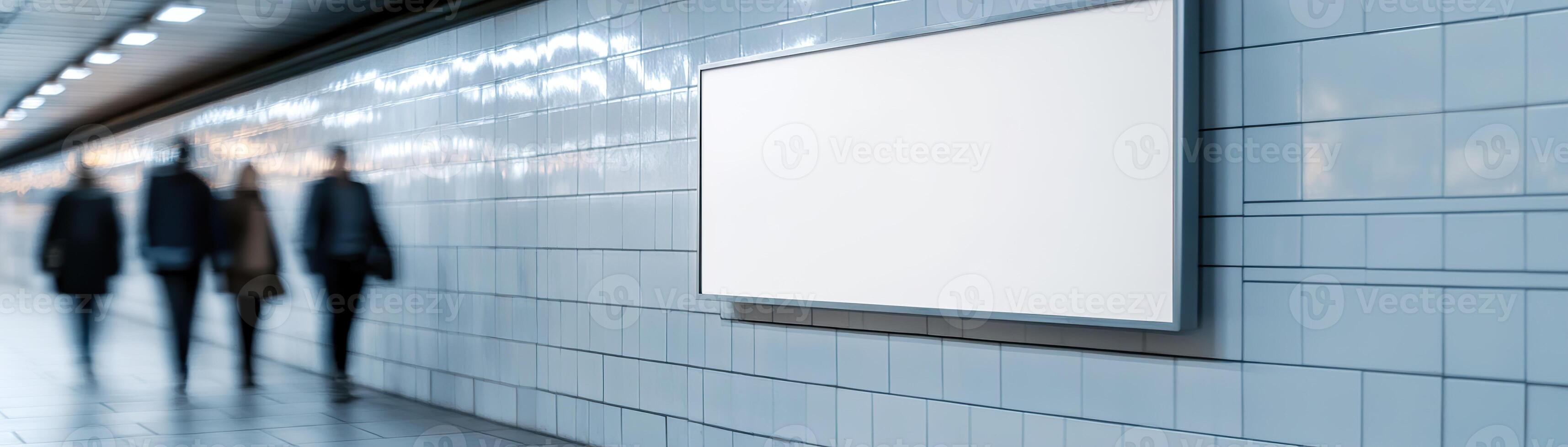A sleek blank billboard is mounted on the tiled wall of a contemporary subway station. Commuters walk by, adding to the vibrant, dynamic atmosphere of daily transit life photo