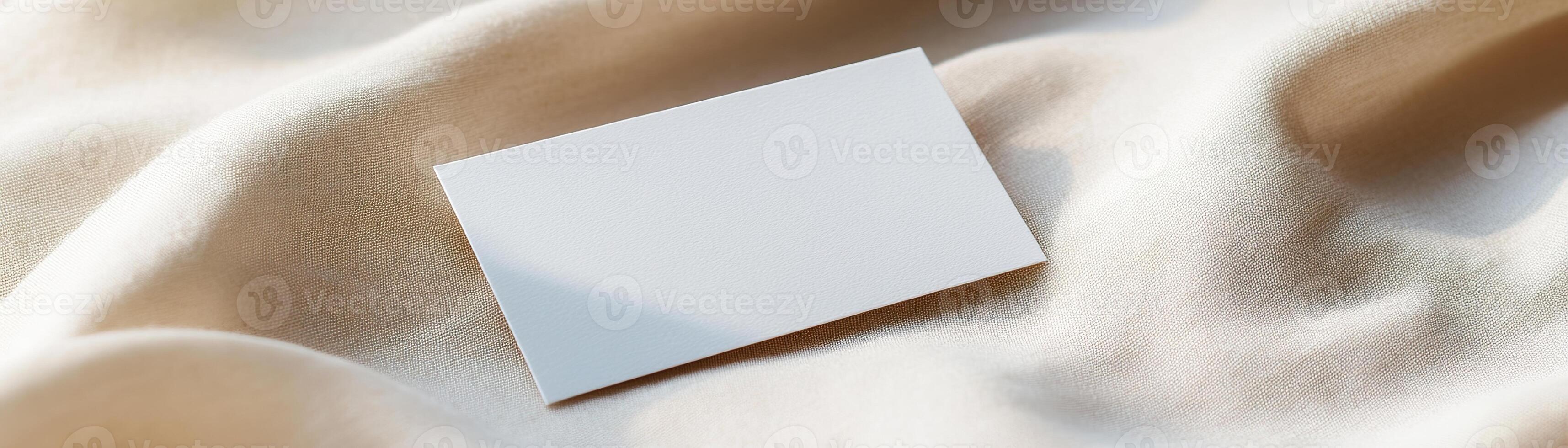 A blank business card rests on soft linen, showcasing subtle folds and shadows. The warm, earthy backdrop enhances its minimalist appeal, ideal for eco-friendly branding photo