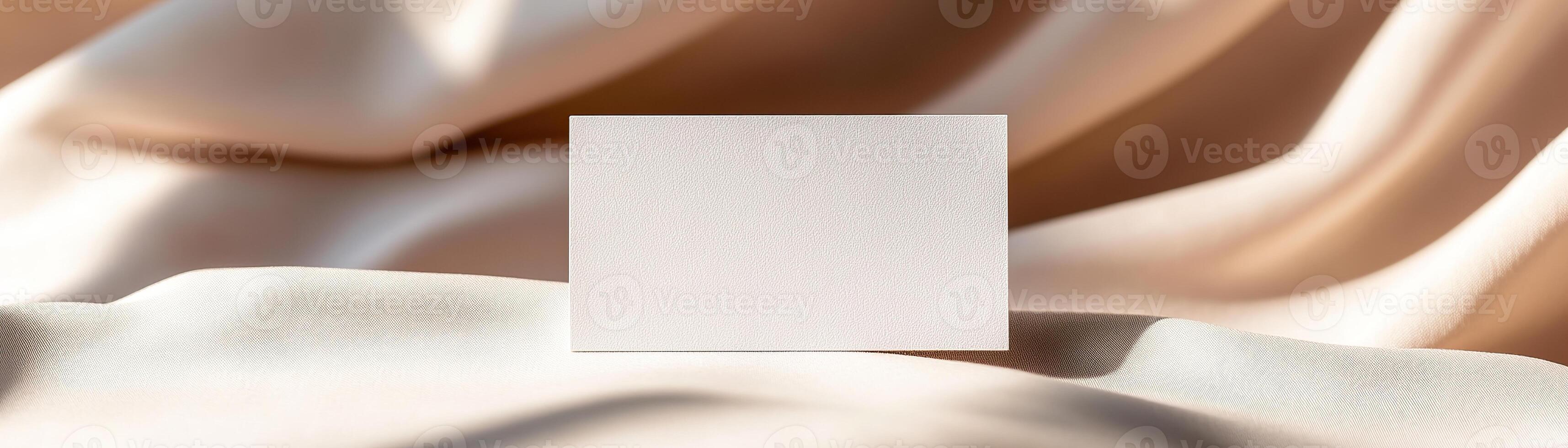 A blank business card rests on soft linen fabric with subtle folds, creating natural shadows. The warm earthy tones in the background enhance the refined and inviting atmosphere photo