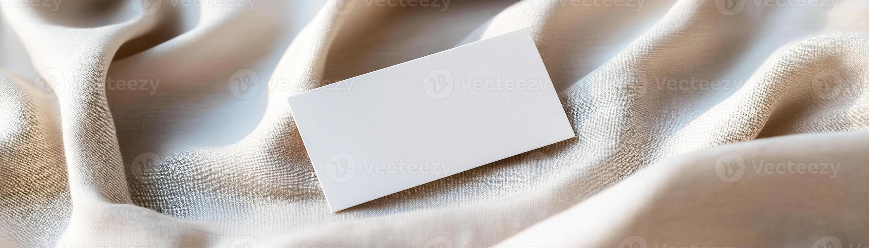 A blank business card rests on soft, wrinkled linen, casting delicate shadows, and surrounded by a softly blurred, warm background conveying a refined and natural atmosphere photo