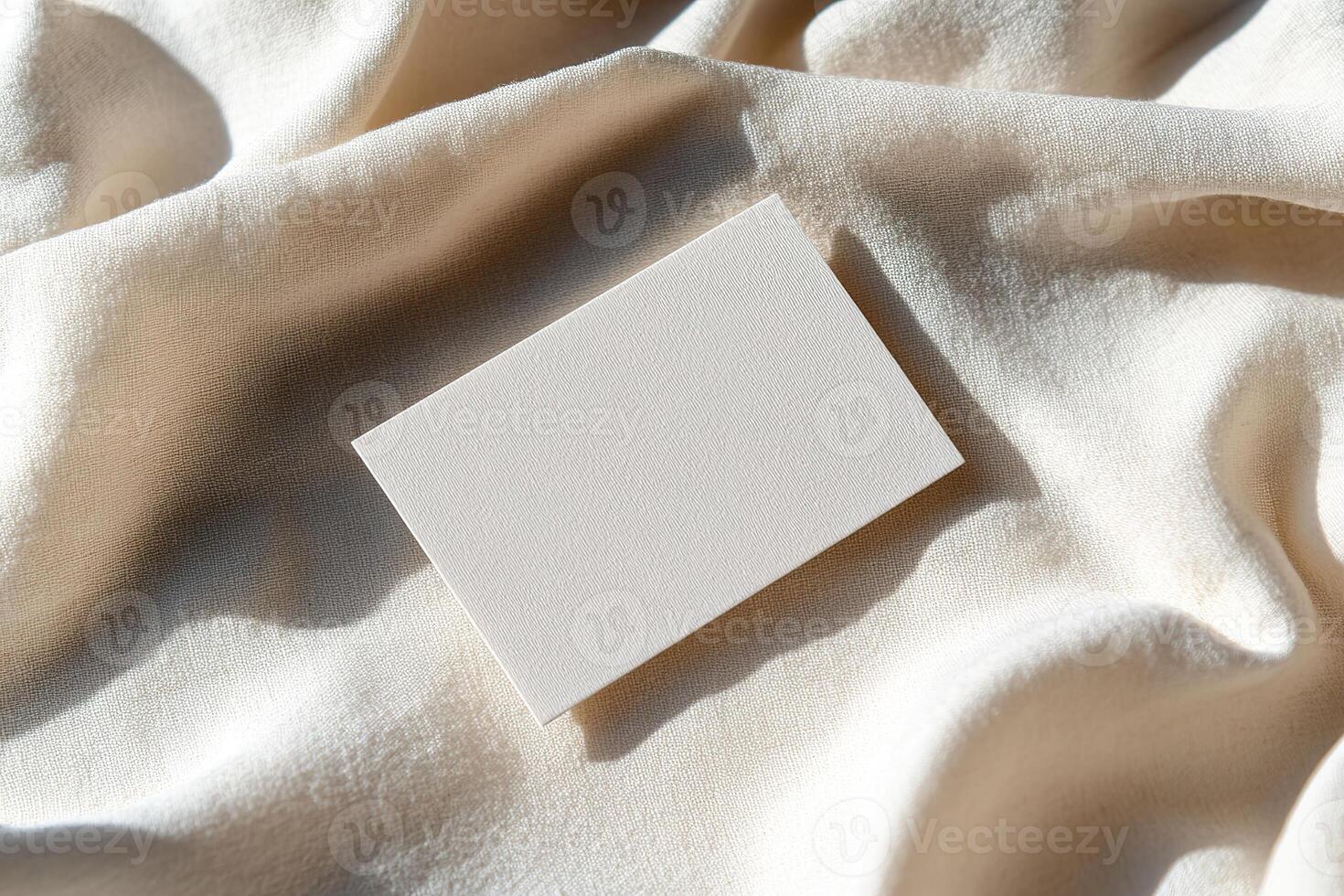 A blank business card is placed on gently wrinkled linen fabric, creating soft shadows. The warm earthy backdrop enhances the natural, refined aesthetic, ideal for eco-friendly brands photo