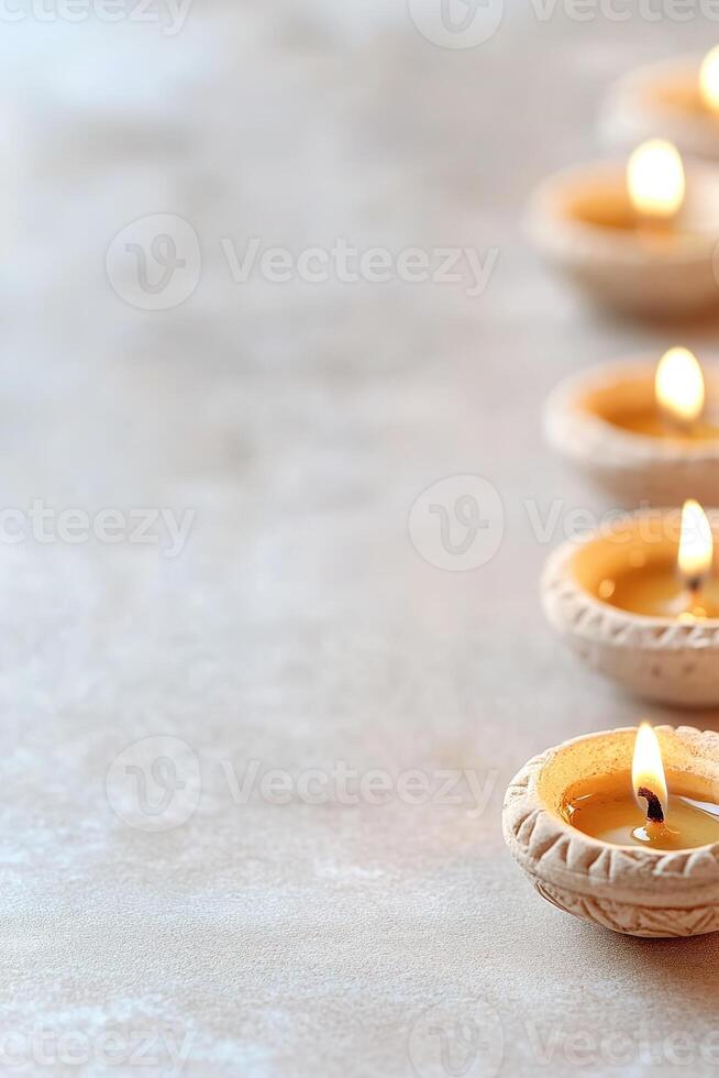 Delicate traditional diwali oil lamps illuminate the bottom edge of the frame, surrounded by detailed Rangoli designs set against a neutral background, creating a warm festive atmosphere photo
