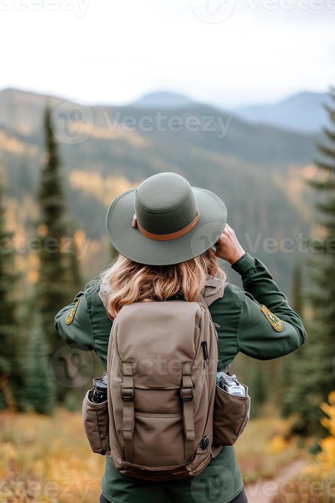 A park ranger in a green uniform stands on a beautiful hiking trail, holding binoculars to observe wildlife photo