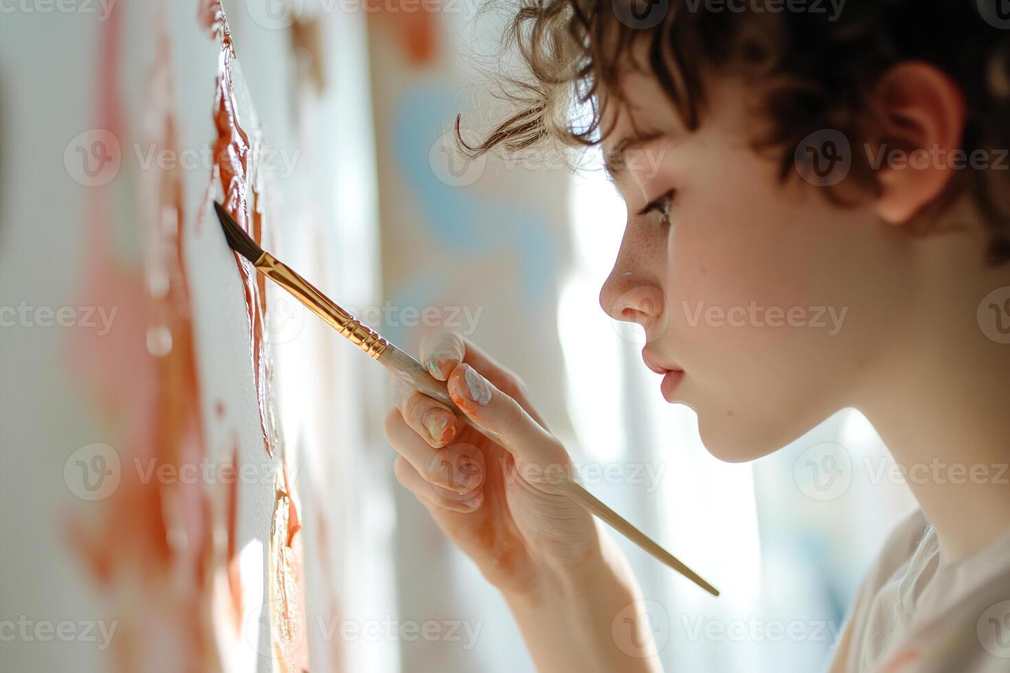 In a bright art studio, a young artist focuses intently on their colorful canvas, paintbrush in hand. The environment is filled with splashes of paint and unfinished pieces that inspire creativity photo