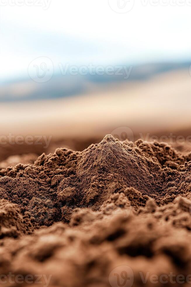 Close-up view of freshly plowed dark brown soil illuminated by soft sunlight, highlighting the rich texture against softly blurred rolling hills in the background photo