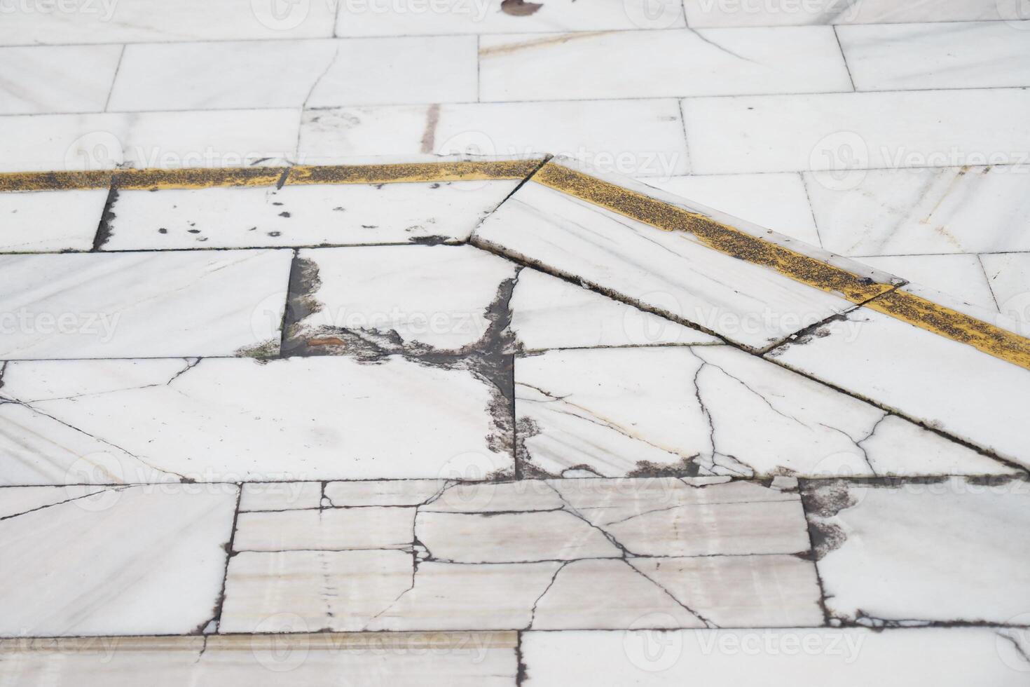 Cracked marble floor with a yellow line in an indoor space photo
