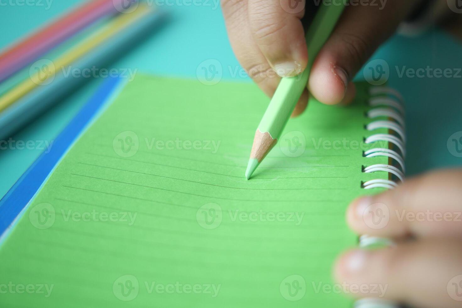 Writing with green pencil on lined notebook in a bright setting photo