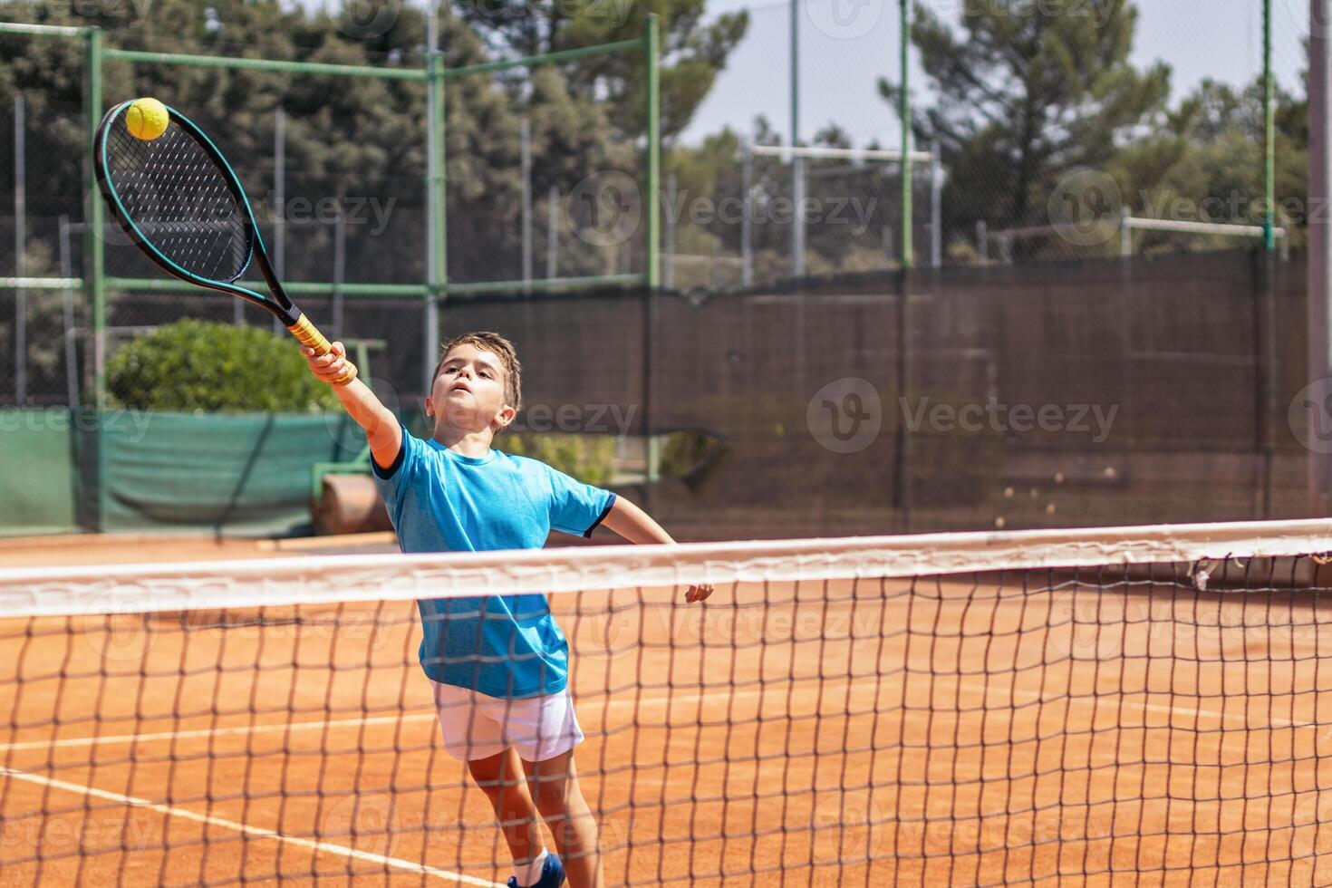 Little boy playing tennis on a dirt court photo