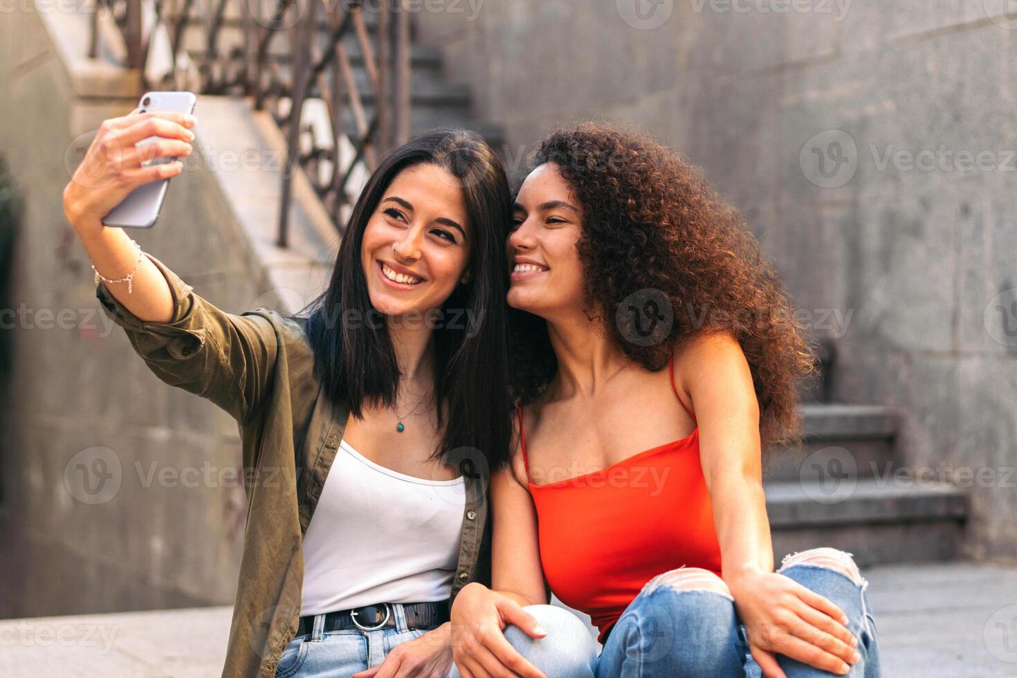 two beautiful women sitting on a stairs taking a selfie photo
