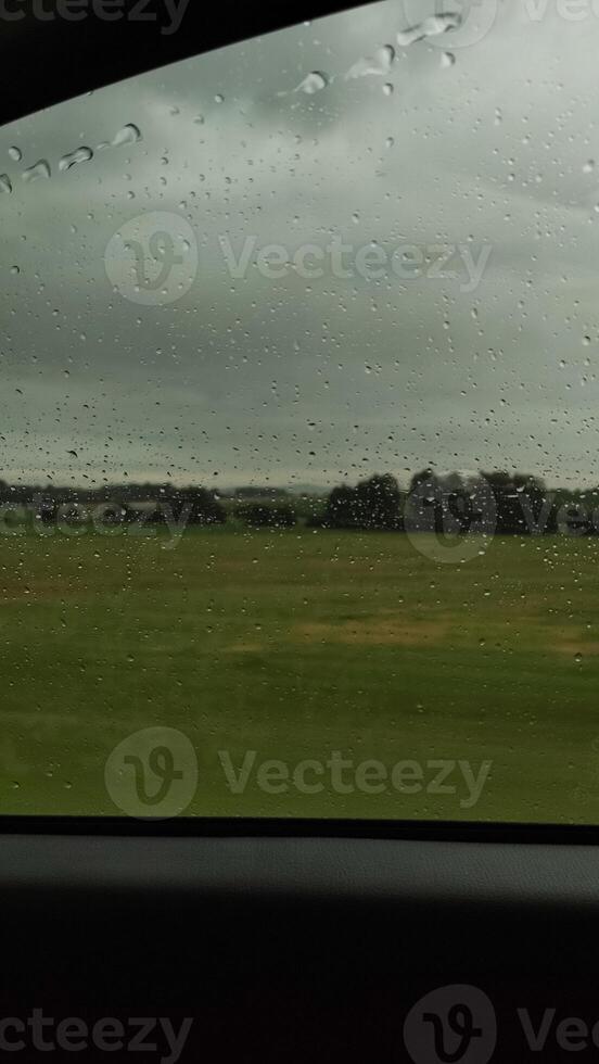 Rain falling on car window overlooking green field in czech republic photo