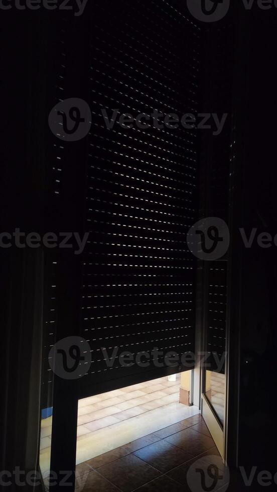 Sliver of sunlight illuminates the tiled floor as it streams through a half open door, contrasting with the darkness of the room's interior photo