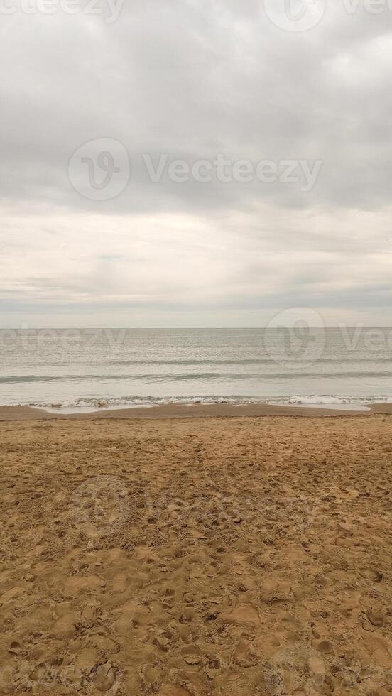 Waves gently caress the sandy shore of bibione beach in veneto, italy, under a soft, cloudy sky photo