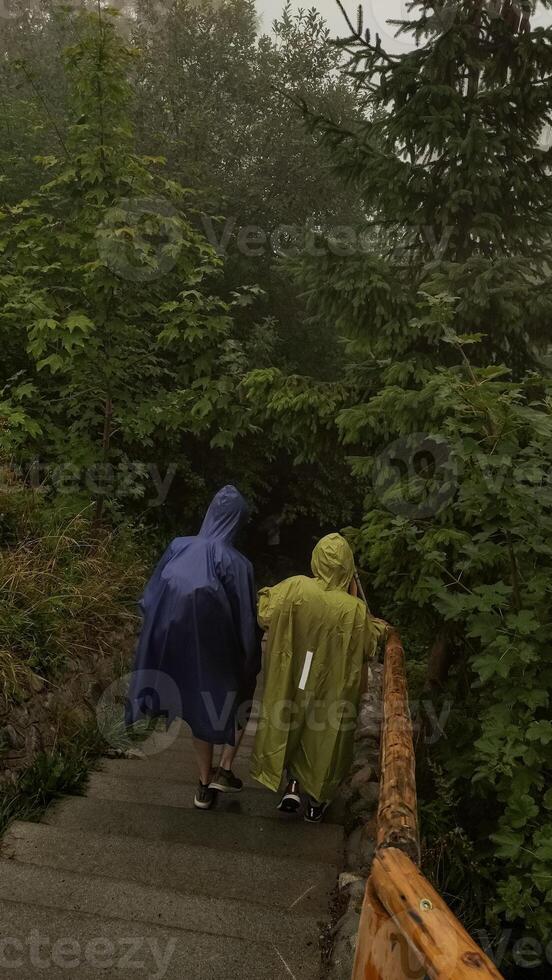 Hikers walking down stairs in rain wearing ponchos in strbske pleso, high tatras mountains photo