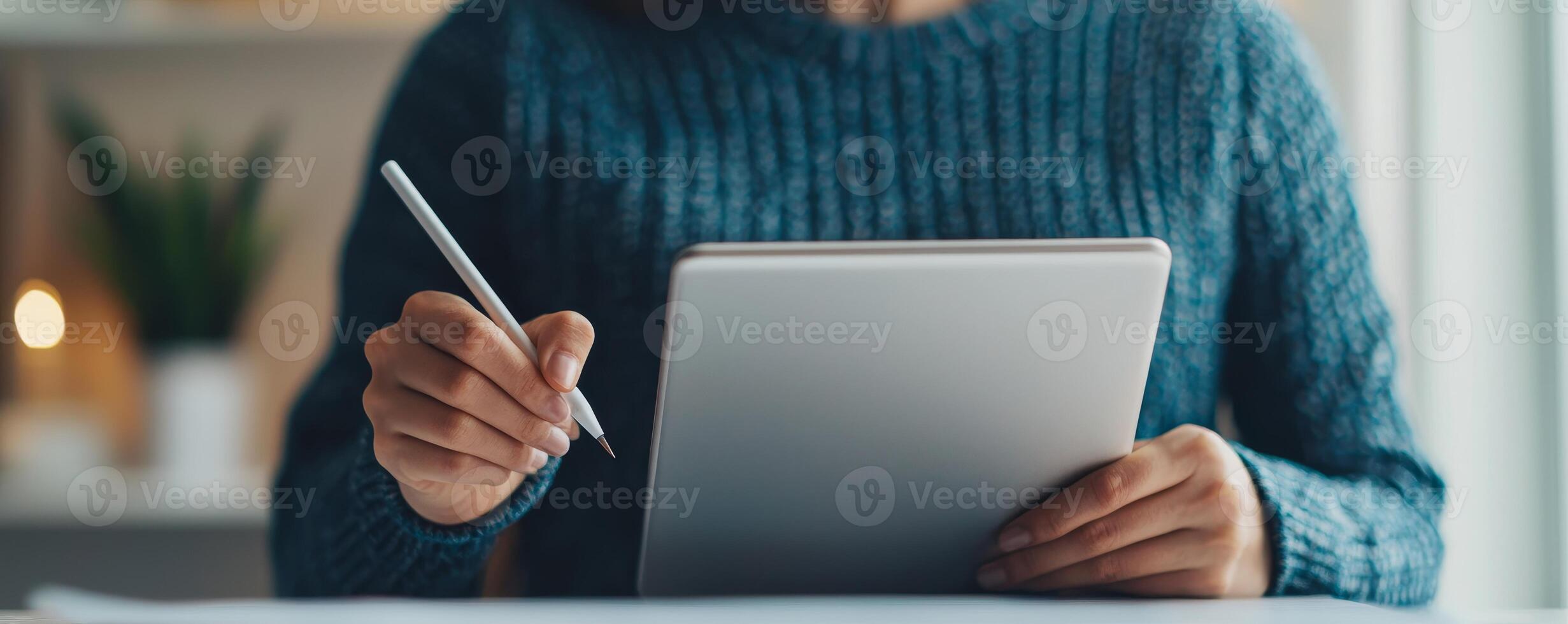 Digital transformation e-learning courses concept. Person writing on a tablet with a pen, dressed in a cozy sweater, in a softly lit environment. photo