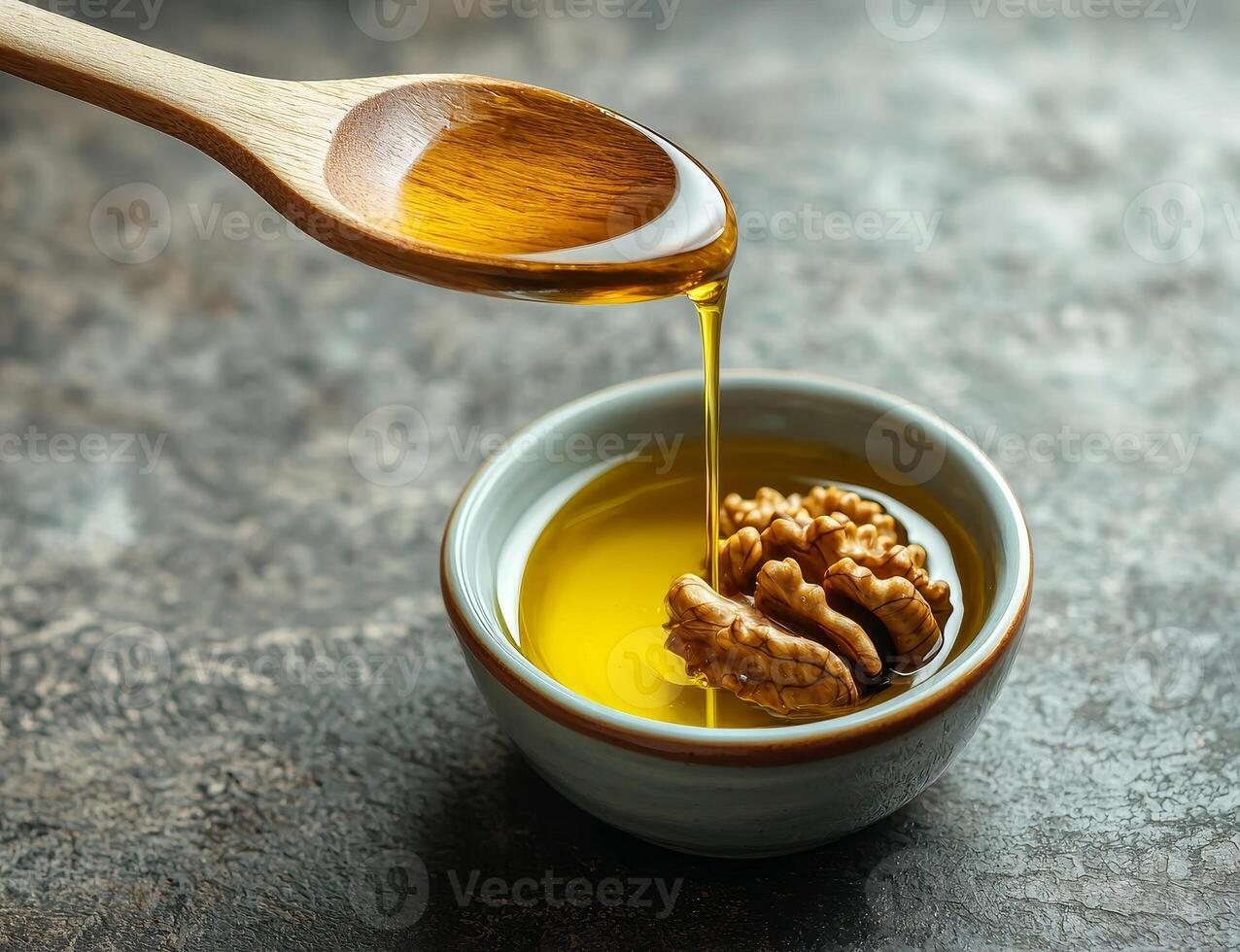 Walnut oil in glass bottle concept. Golden oil being drizzled from a wooden spoon into a small bowl with walnuts. photo