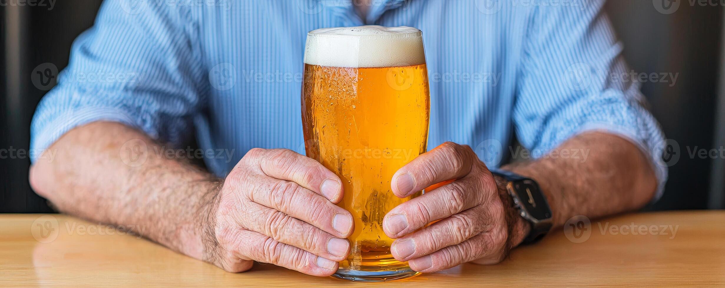 A person holding a glass of beer, showcasing its golden color and frothy top, with hands resting on a wooden surface. photo
