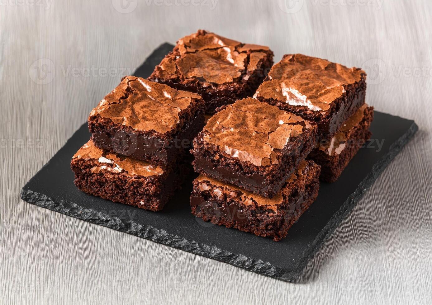 Rich brownie with chocolate chunks concept. Deliciously baked brownies stacked on a slate board, showcasing a rich chocolate texture with a crispy top layer. photo
