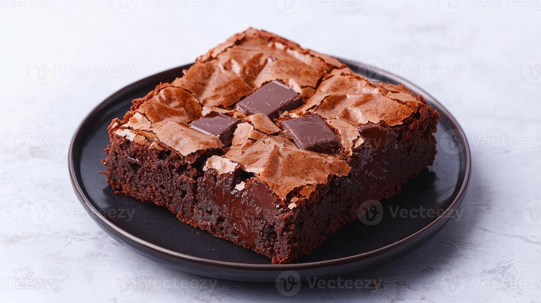 Rich brownie with chocolate chunks concept. A rich, fudgy chocolate brownie topped with chunks of chocolate, served on a black plate against a light background. photo
