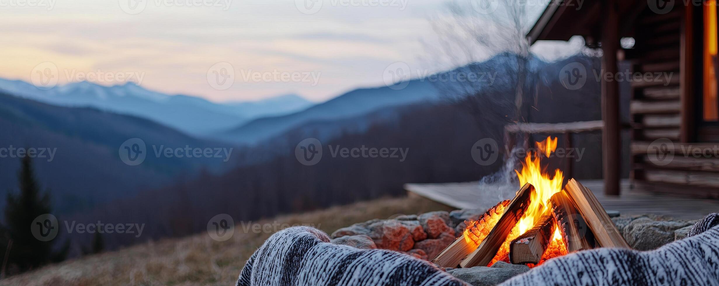 Girlfriend getaways for travel concept. Cozy campfire burns in the foreground, with a rustic cabin nearby and majestic mountains in the background, creating a serene outdoor atmosphere at dusk. photo