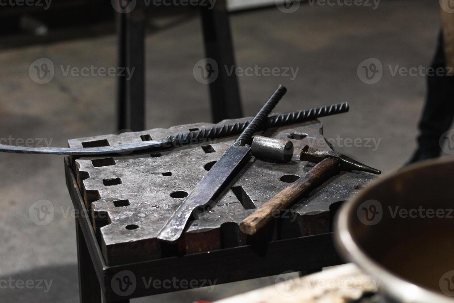 A blacksmith's tools on a table with a pot of hot liquid photo