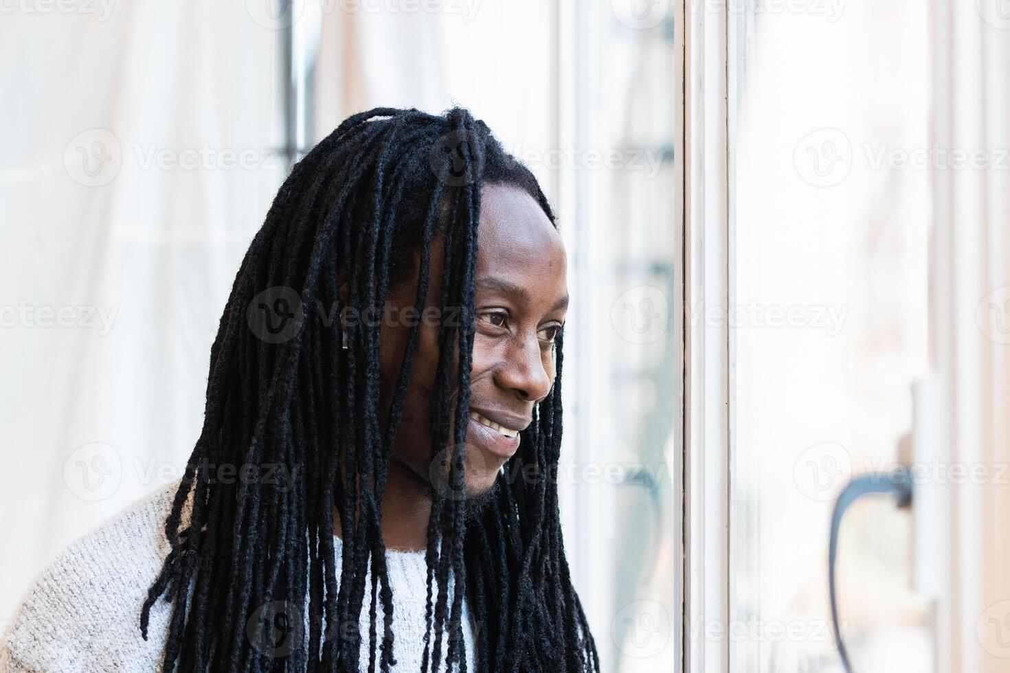 A man with dreadlocks standing in front of a window photo