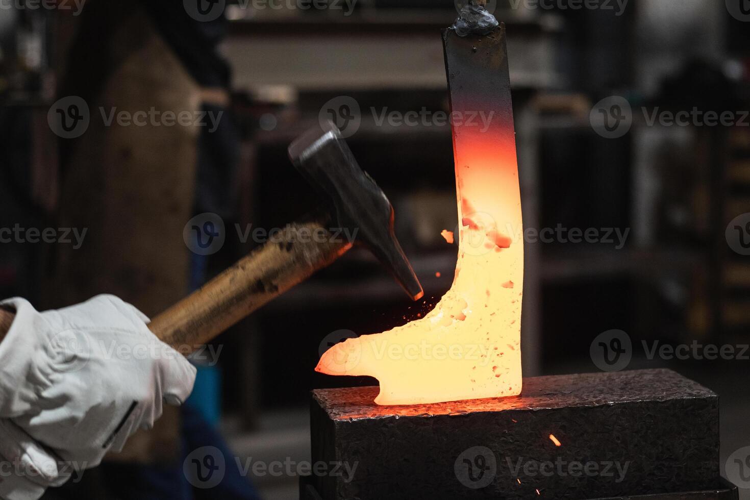 A person is holding a hammer and a piece of metal photo
