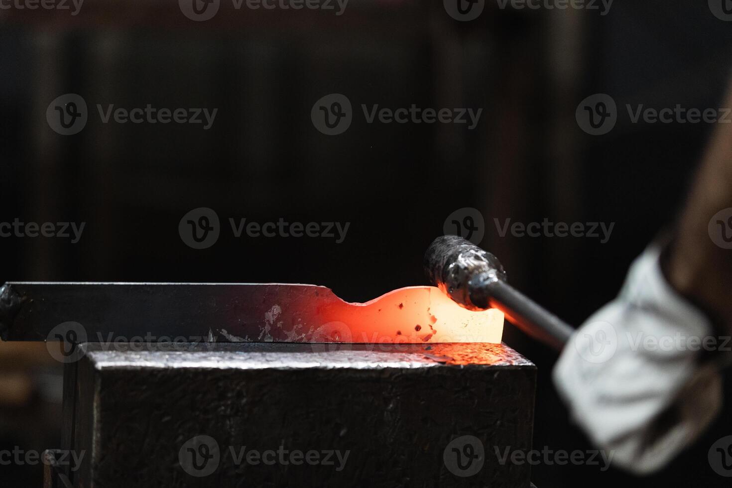 A person is holding a hammer and a red hot piece of metal photo