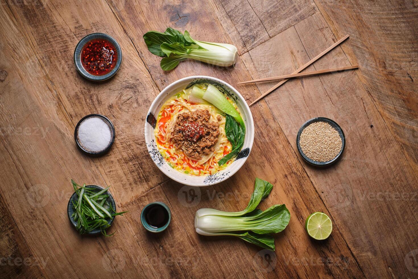 A bowl of noodles with vegetables and chopsticks on a wooden table photo