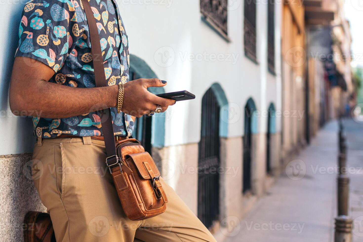 A man with a backpack and a cell phone leaning against a wall photo