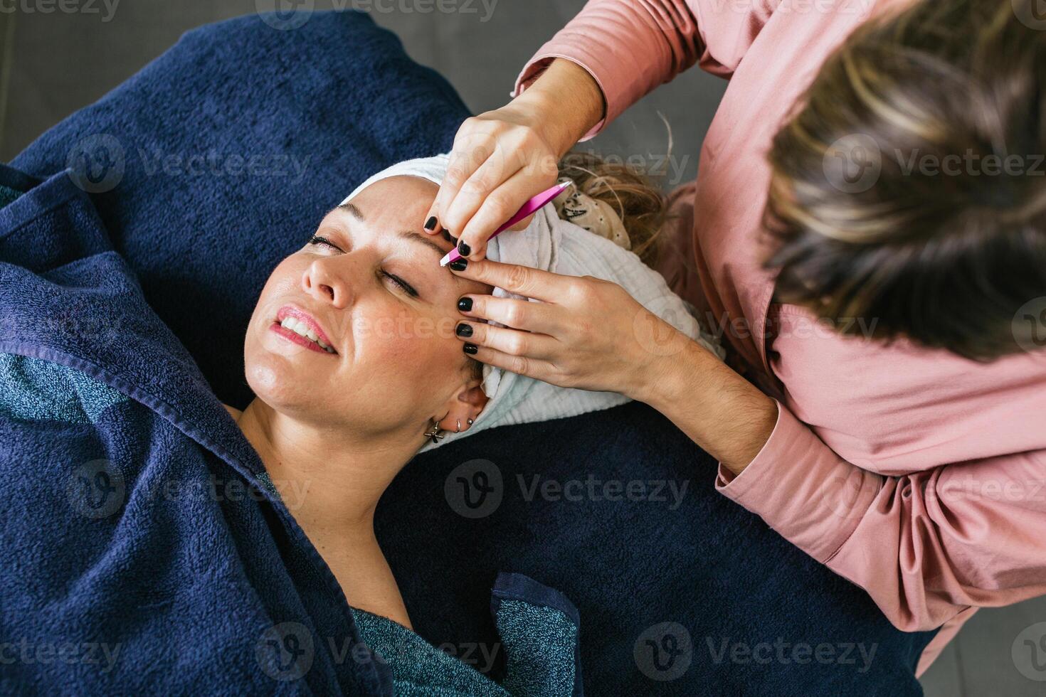 Unrecognizable beautician plucking eyebrows on face of woman in salon photo