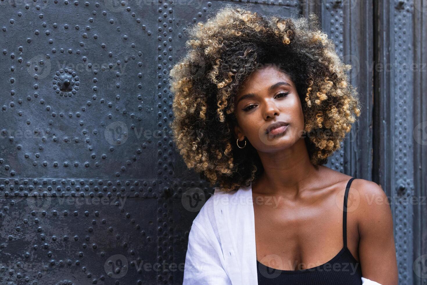 Stylish black woman sitting on concrete steps near gates photo