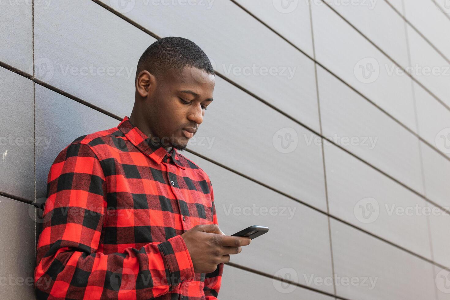 Serious black man using smartphone against gray wall photo