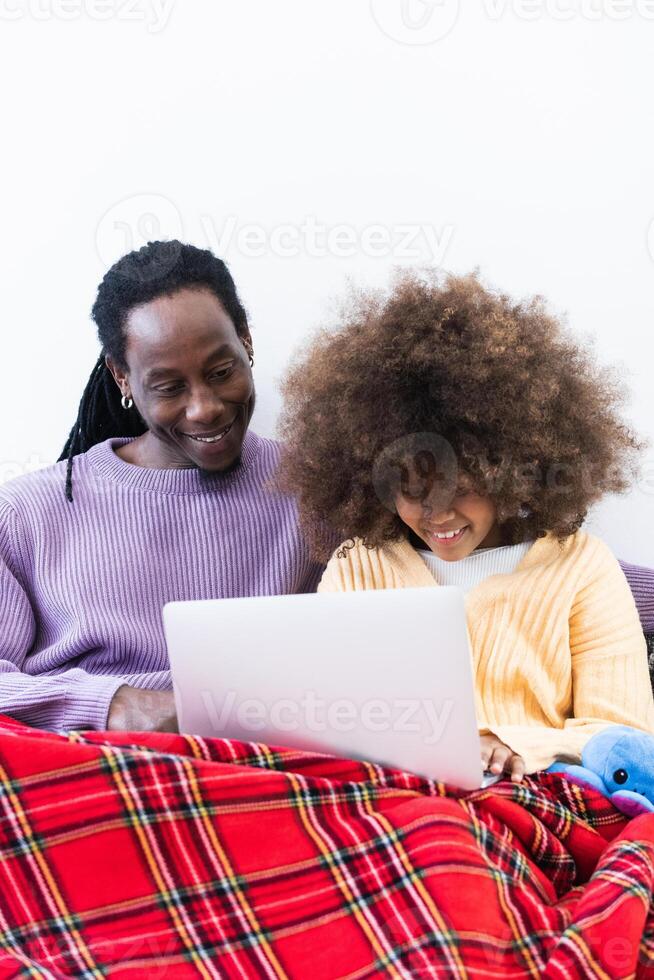 Black father browsing laptop with daughter under plaid photo